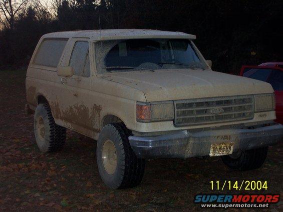 Tan Ford Bronco, 1987 model year, covered in mud, 3q front view