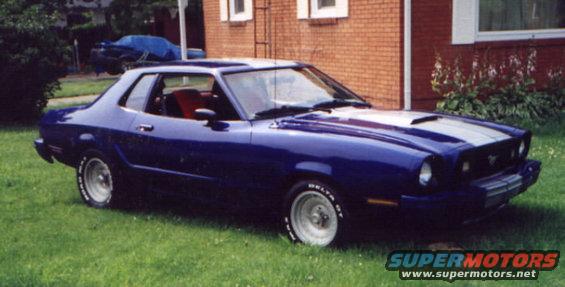 Blue 1977 Ford Mustang II coupe with silver racing stripes parked on grass