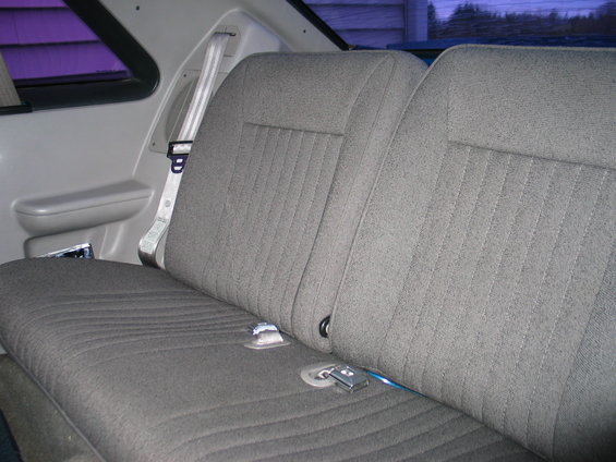Rear bench seat with grey fabric upholstery and white seatbelts