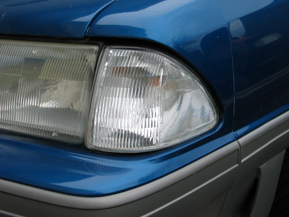 Close-up of blue car's front corner, showing headlight and part of bumper