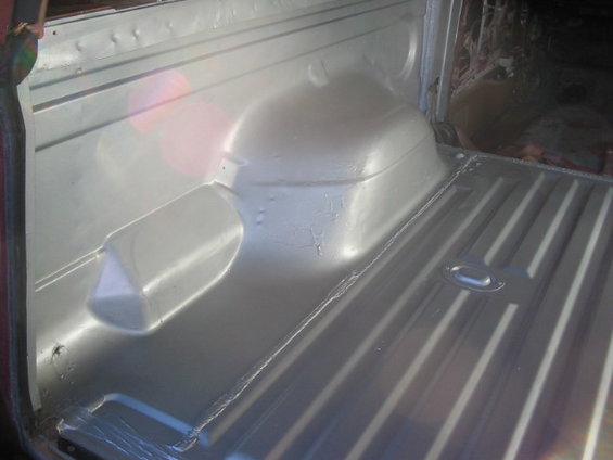 Interior of a vehicle's cargo area, showing the floor and wheel wells. The metal surfaces appear to be painted silver
