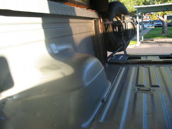 Spare tire mounted on bracket inside a truck bed, viewed from the side
