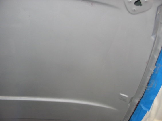 Underside of a car hood, painted gray, with blue tape on the right edge