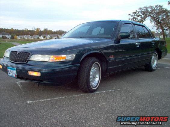 Dark green 1995 Mercury Grand Marquis parked on asphalt with a tree and houses in the background