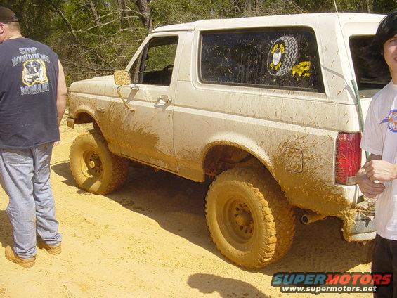 Mud-covered 1989 Ford Bronco parked off-road with two people nearby