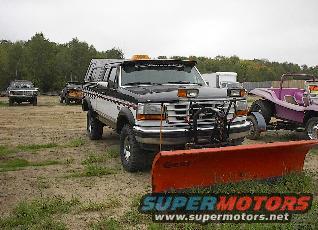 Ford F-series truck with a plow attached, parked outside. Other vehicles visible in background