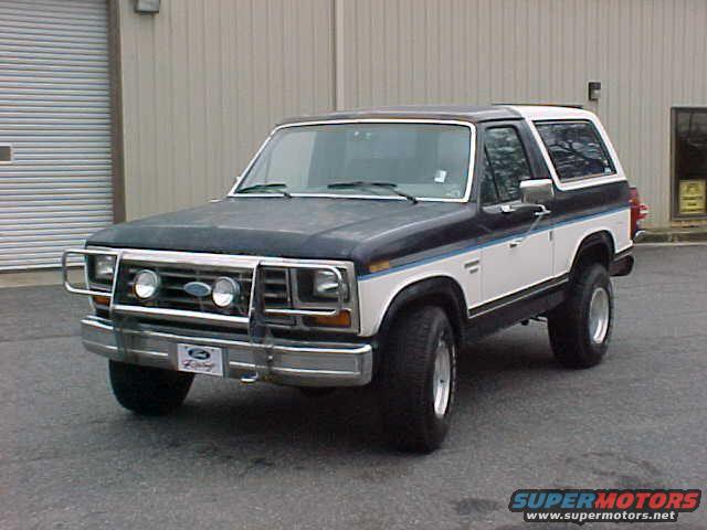 Ford Bronco parked in front of a building. It has a dark blue and white paint scheme with a chrome bumper and grille guard