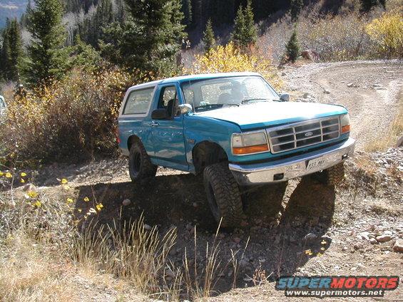 Blue Ford Bronco on a rocky dirt road with trees in the background