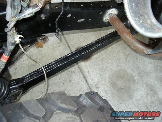 Black painted suspension arm and rusty exhaust pipe near a large tire tread