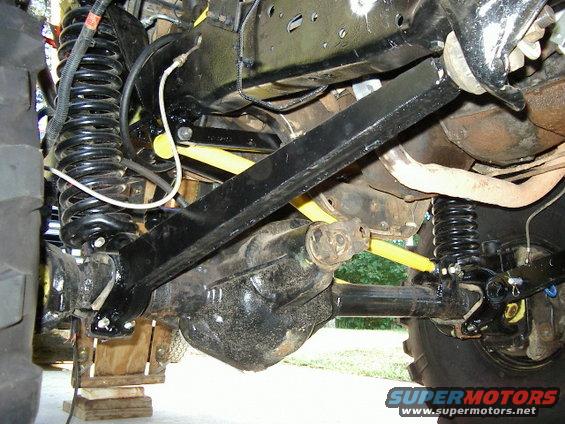 Close-up of a vehicle's front axle, differential, springs, and control arms. Some yellow shocks are visible