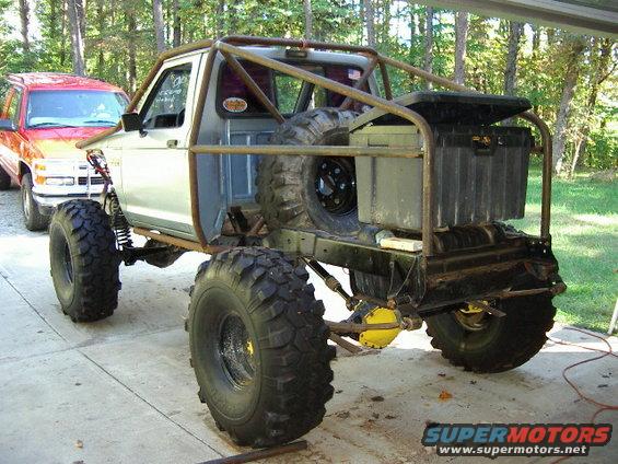 Customized pickup truck with roll cage and large tires parked next to a red SUV