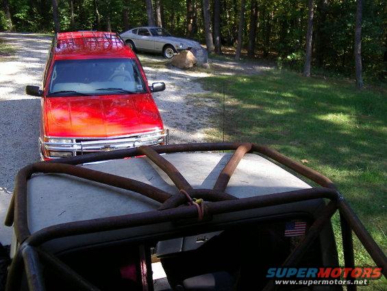 Red SUV with chrome grille and silver coupe parked on gravel driveway