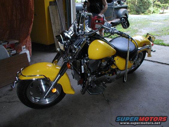 Yellow motorcycle with chrome accents and black seat, parked indoors