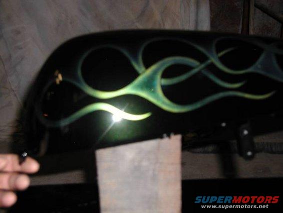 Black motorcycle fuel tank with green and yellow flame graphics. A hand is visible on the left