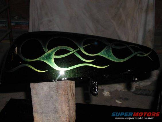Black motorcycle fuel tank with green flame graphics, resting on a wooden block