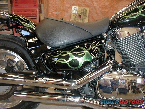 Black motorcycle with green flame graphics on the side panel and fender. Chrome exhaust pipes are visible
