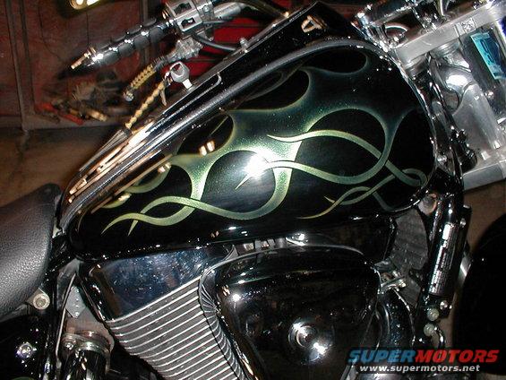 Motorcycle fuel tank with black and green flame paint job. Chrome engine parts visible
