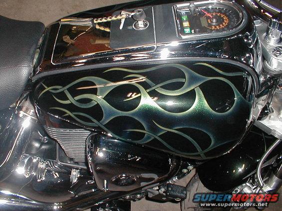 Motorcycle fuel tank with black and green flame paint, chrome accents, and a speedometer
