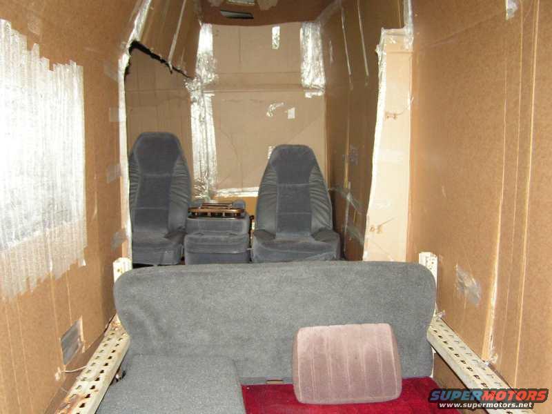 Interior of a van with cardboard walls, two rows of seats, and a bench seat