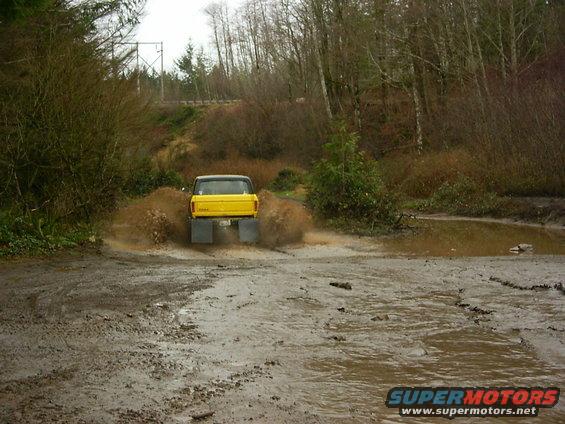 Yellow pickup truck with large mud flaps driving through a muddy puddle