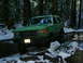 1990 Ford Bronco - Green 1990 Ford Bronco navigates a snowy, wooded trail with water and rocks.