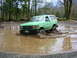 1990 Ford Bronco - A green 1987 Ford Bronco navigates a muddy obstacle course in a wooded area.