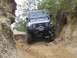 1990 Ford Bronco - This blue Jeep Wrangler is shown tackling a challenging off-road trail with steep inclines and rocky terrain.