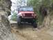 1990 Ford Bronco - A red Jeep Wrangler tackles a challenging off-road path with steep, eroded sides.