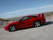 1999 Mitsubishi 3000GT - Side view of a red 1999 Mitsubishi 3000GT sports car on a dirt road.