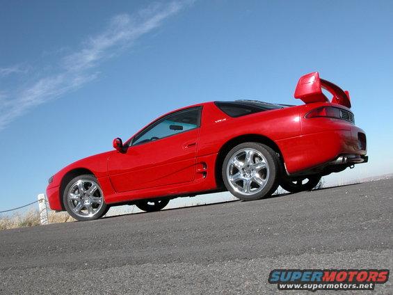 Red 1999 Mitsubishi 3000GT parked on a roadside with a blue sky