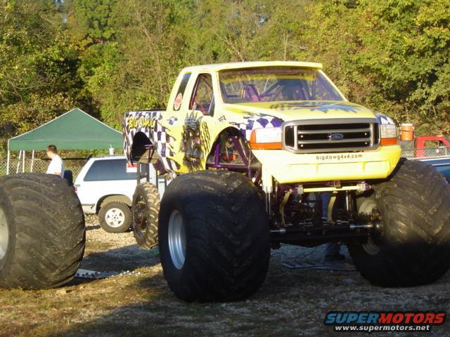 Yellow monster truck with large tires and checkered flag graphics, front view