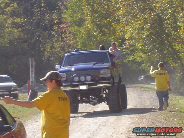 Blue lifted truck with large tires and off-road lights, seen from a 3/4 front angle
