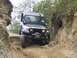 1990 Ford Bronco - Jeep Wrangler tackling a challenging off-road course with steep dirt banks and rocks.