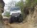 1990 Ford Bronco - A white Jeep Wrangler tackles a challenging off-road trail, its front end visible as it maneuvers through a narrow, rocky passage.