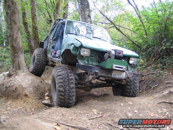 Green modified off-road SUV with large tires navigating a dirt trail