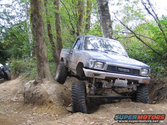 Toyota pickup truck with lifted suspension navigating an off-road trail, another vehicle visible behind it