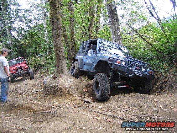 Blue Jeep Wrangler and red Jeep CJ on a wooded trail. Blue Jeep is going uphill