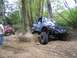 1990 Ford Bronco - Two off-road vehicles navigate a steep, wooded trail with one vehicle climbing over an obstacle.