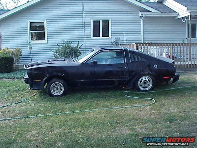 Black 1978 Ford Mustang II coupe with louvers on the rear window, seen from the side in a grassy yard