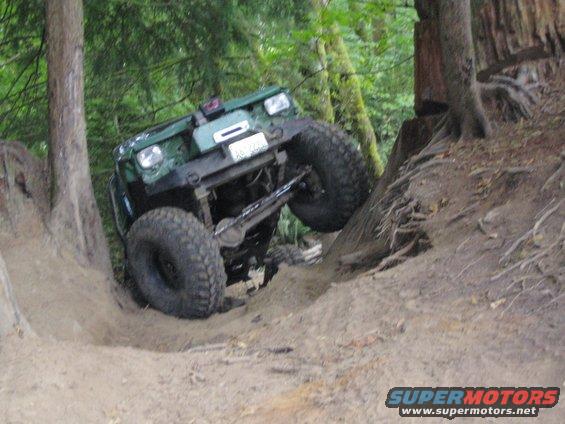 Green off-road vehicle with large tires climbing a dirt hill, front end tilted