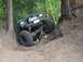 1990 Ford Bronco - A green off-road vehicle navigates a steep dirt incline in a wooded area.