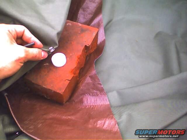 Hand holding a tool, pressing a snap onto a red brick and brown fabric