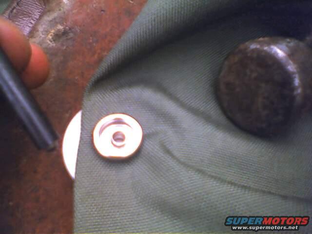 Close-up of a snap fastener being attached to green fabric with a tool. A round metal object is also visible