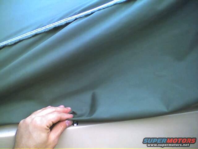 Hand securing a dark green car cover with a clip over a tan surface