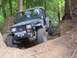 1990 Ford Bronco - A Jeep Wrangler navigates a steep, wooded trail with its front tires digging into the dirt.