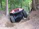 1990 Ford Bronco - An orange Jeep Wrangler navigates a challenging off-road trail through a forest.
