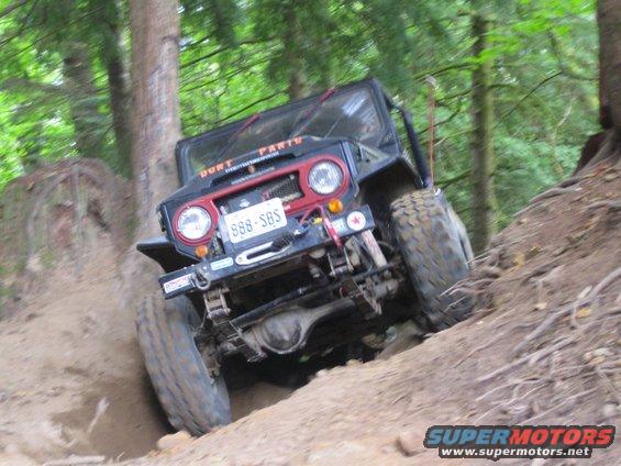 Off-road vehicle with license plate 888-SBS climbing a steep dirt incline in a wooded area