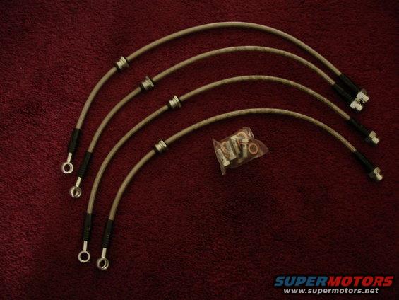 Four braided brake lines with banjo fittings and a bag of assorted fittings on a red textured surface