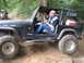 1990 Ford Bronco - A black Jeep Wrangler navigates an off-road trail with two people inside.