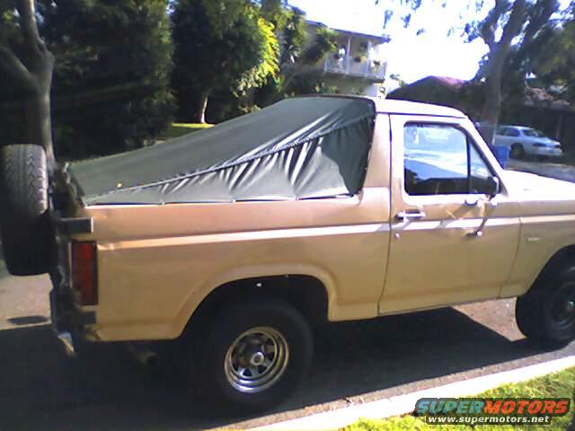 Tan 1980s Ford Bronco with a dark green soft top and a spare tire mounted on the rear tailgate